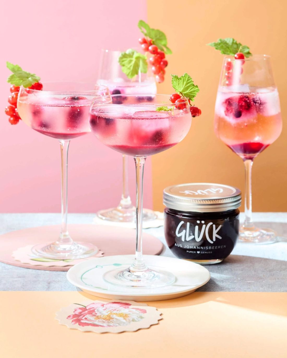 Schwarze Johannisbeere Spritz garniert mit Johannisbeeren. Daneben ein Glas GLÜCK aus Johannisbeeren.