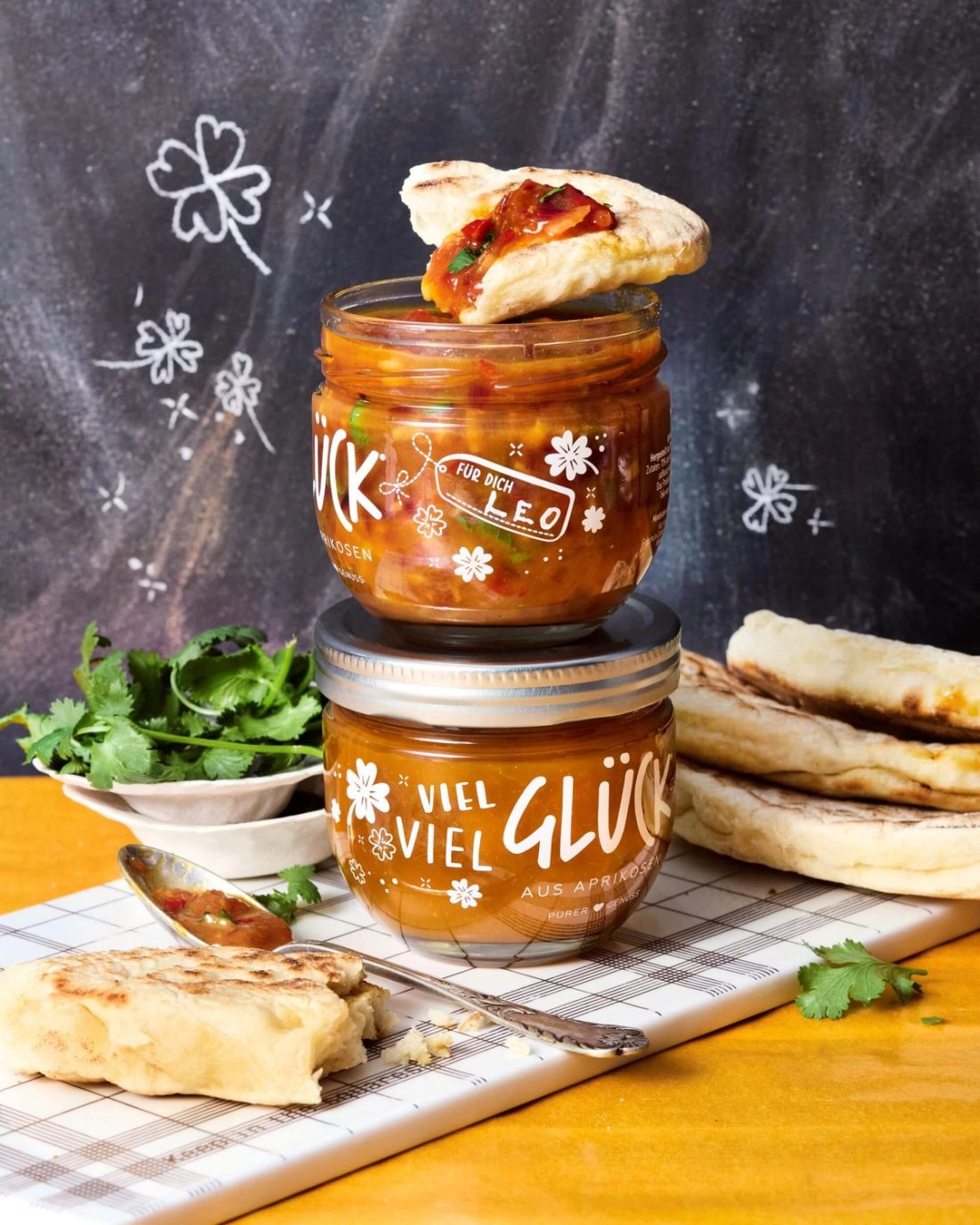 Aprikosen-Chutney im GLÜCK Glas. Daneben Naan-Brot garniert mit Chutney. Dabei steht ein volles Glas GLÜCK aus Aprikosen.