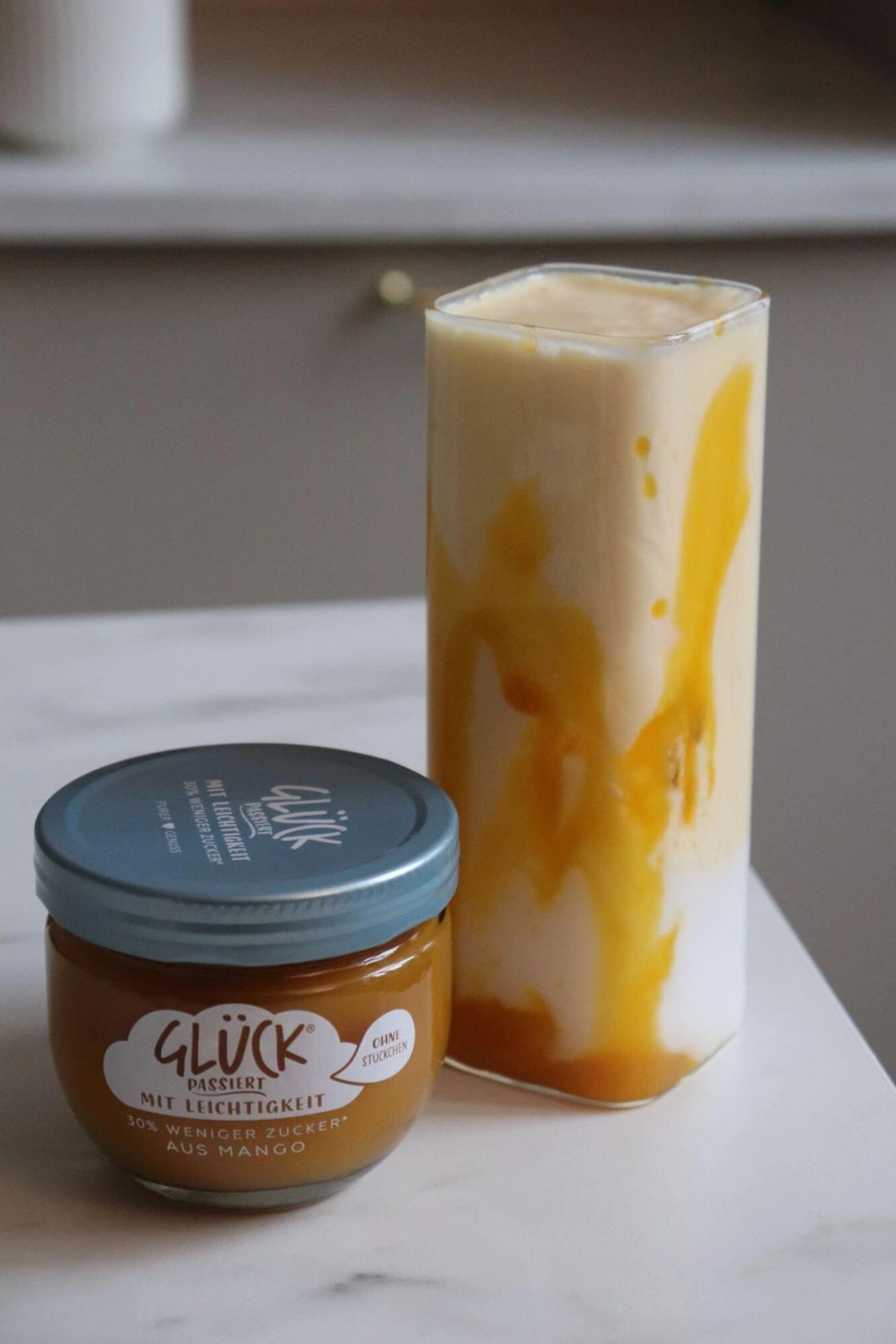 Mango-Kokos-Kefir im Glas neben einem Glas GLÜCK passiert mit Leichtigkeit aus Mango