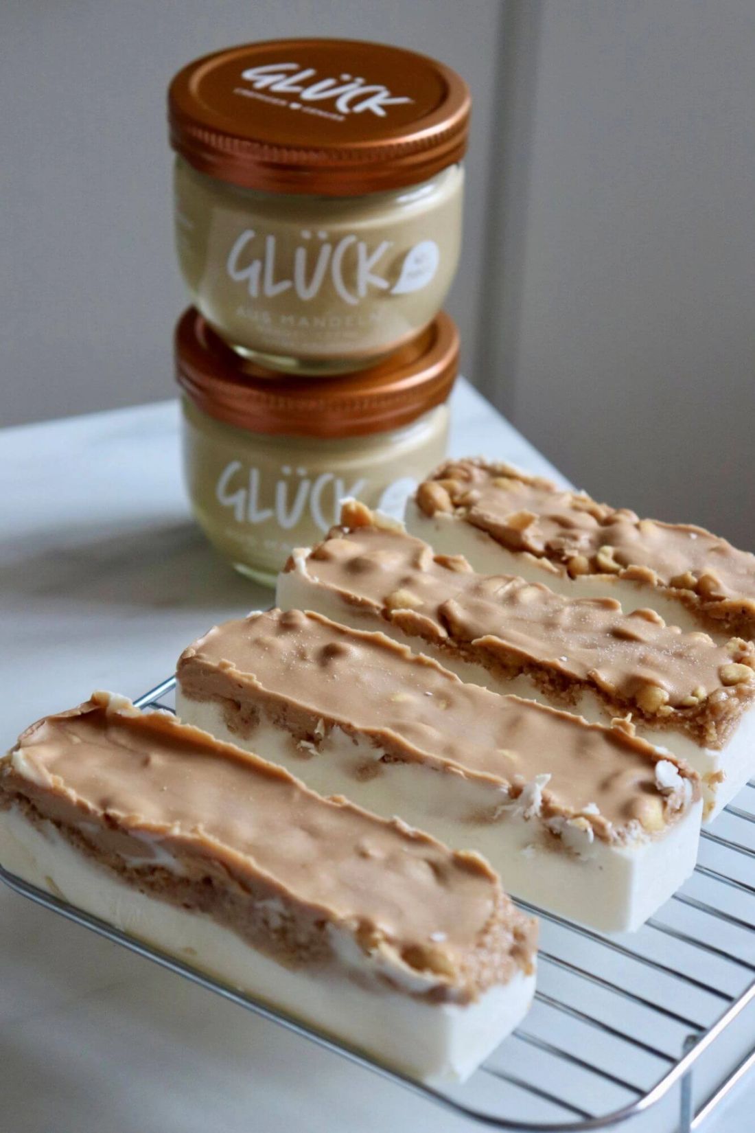 Hazelnut Peanut Bars auf einem Gitter. Im Hintergrund zwei Gläser GLÜCK aus Haselnüssen