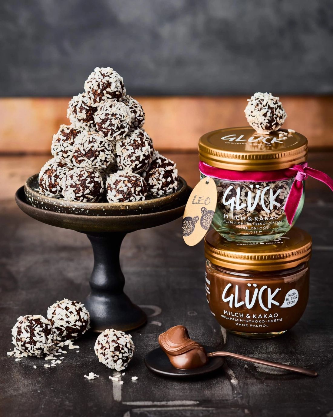 Chokladbollar Schokokugeln mit Kokosflocken auf einem Teller und in einem GLÜCK Glas. Daneben GLÜCK Milch & Kakao