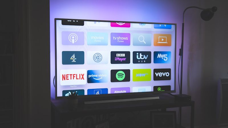 The image features a modern television displaying various streaming service icons on its screen. The setting has ambient lighting that enhances the visual appeal of the display.