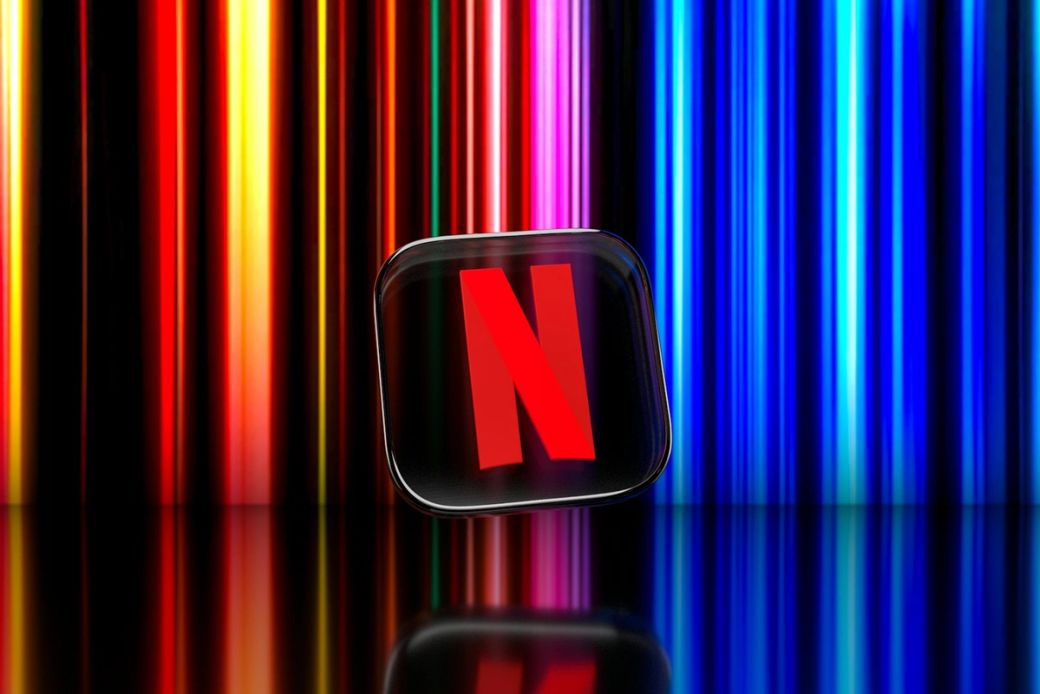 The image features the Netflix logo prominently displayed against a backdrop of vibrant colored vertical stripes. The logo is set on a reflective surface, enhancing its visual impact. — Credit: Photo by Dima Solomin / Unsplash