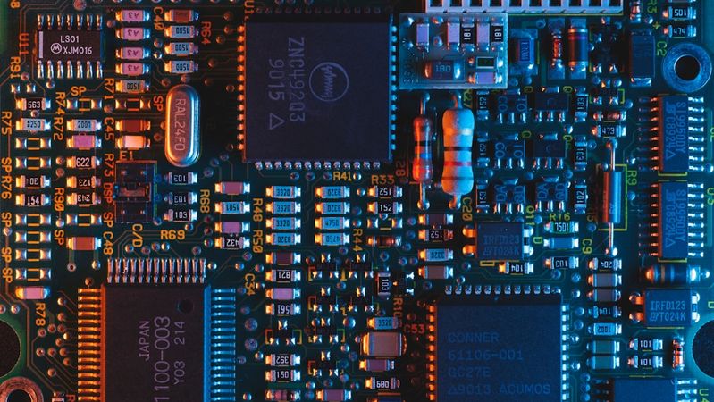 The image depicts a close-up view of a printed circuit board featuring various electronic components, including microchips and capacitors. The intricate details and vibrant colors highlight the complexity of modern electronics.