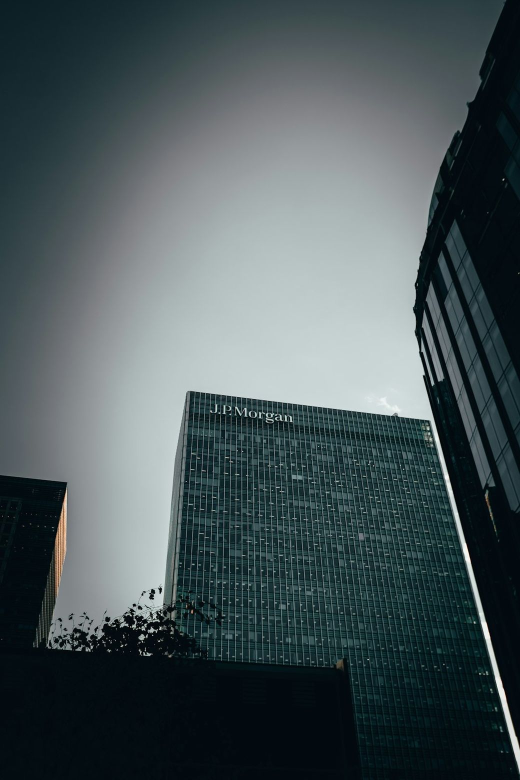 The image features the towering glass facade of a corporate building, prominently displaying the name 'J.P. Morgan' at the top. It is captured from a low angle, creating an imposing view against a clear sky. — Credit: Photo by IKECHUKWU JULIUS UGWU on Unsplash