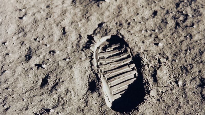 The image shows a clear footprint imprinted in the lunar surface, demonstrating the texture of the moon's regolith. The focus on the boot print indicates human presence during the Apollo missions.