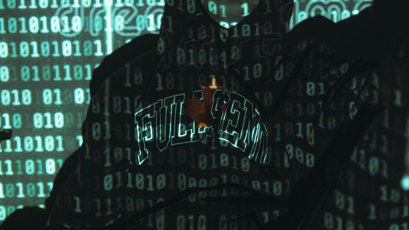 A person wearing a hoodie stands against a backdrop of green binary code, with their face illuminated by the projected numbers. The image evokes themes of technology and digital transformation.