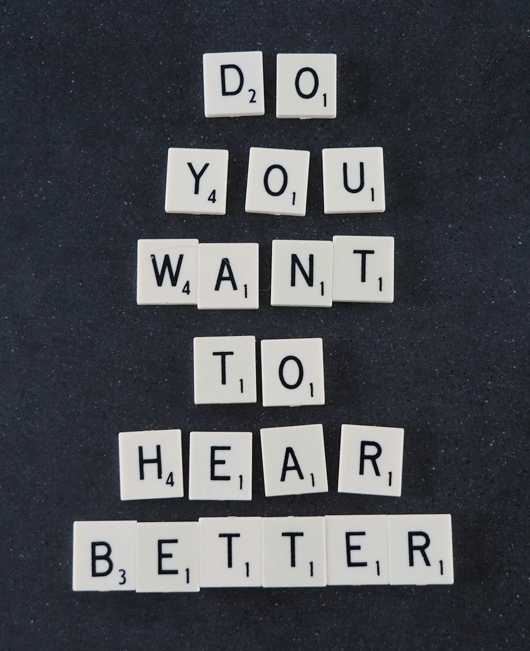The image features a stack of letter tiles arranged to spell out the phrase 'DO YOU WANT TO HEAR BETTER' against a dark background. The tiles are likely made of plastic or a similar material, and the arrangement suggests a playful or interactive concept. — Credit: Photo by Mark Paton on Unsplash