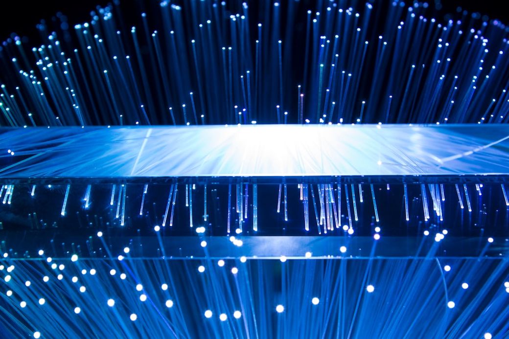 The image depicts a close-up view of a transparent surface emitting numerous thin, glowing strands of light. The bright points of light create a dynamic effect against a dark background, suggesting a technological or futuristic theme. — Credit: Photo by John Adams on Unsplash