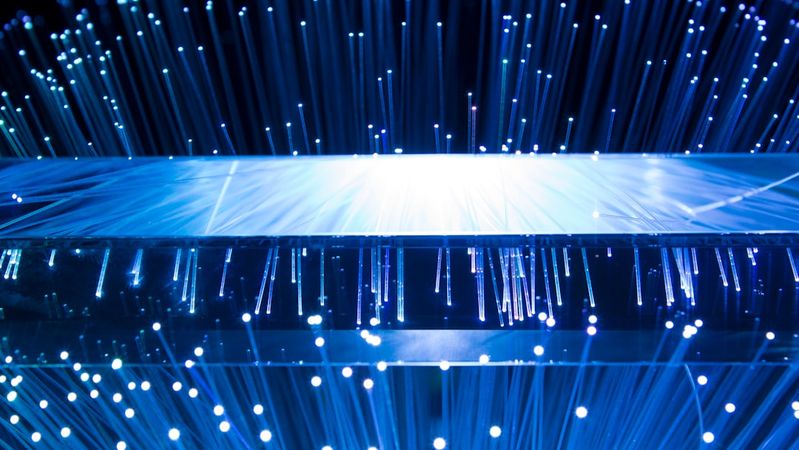The image depicts a close-up view of a transparent surface emitting numerous thin, glowing strands of light. The bright points of light create a dynamic effect against a dark background, suggesting a technological or futuristic theme.