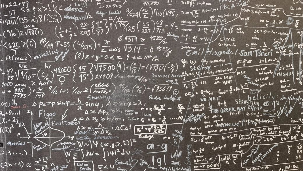 The image features a blackboard or wall covered with handwritten mathematical equations, formulas, and notes. The dense array of symbols and annotations suggests an academic or scientific environment. — Credit: Photo by Thomas T / Unsplash