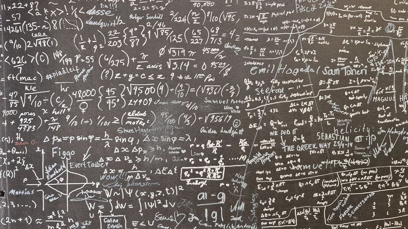 The image features a blackboard or wall covered with handwritten mathematical equations, formulas, and notes. The dense array of symbols and annotations suggests an academic or scientific environment.