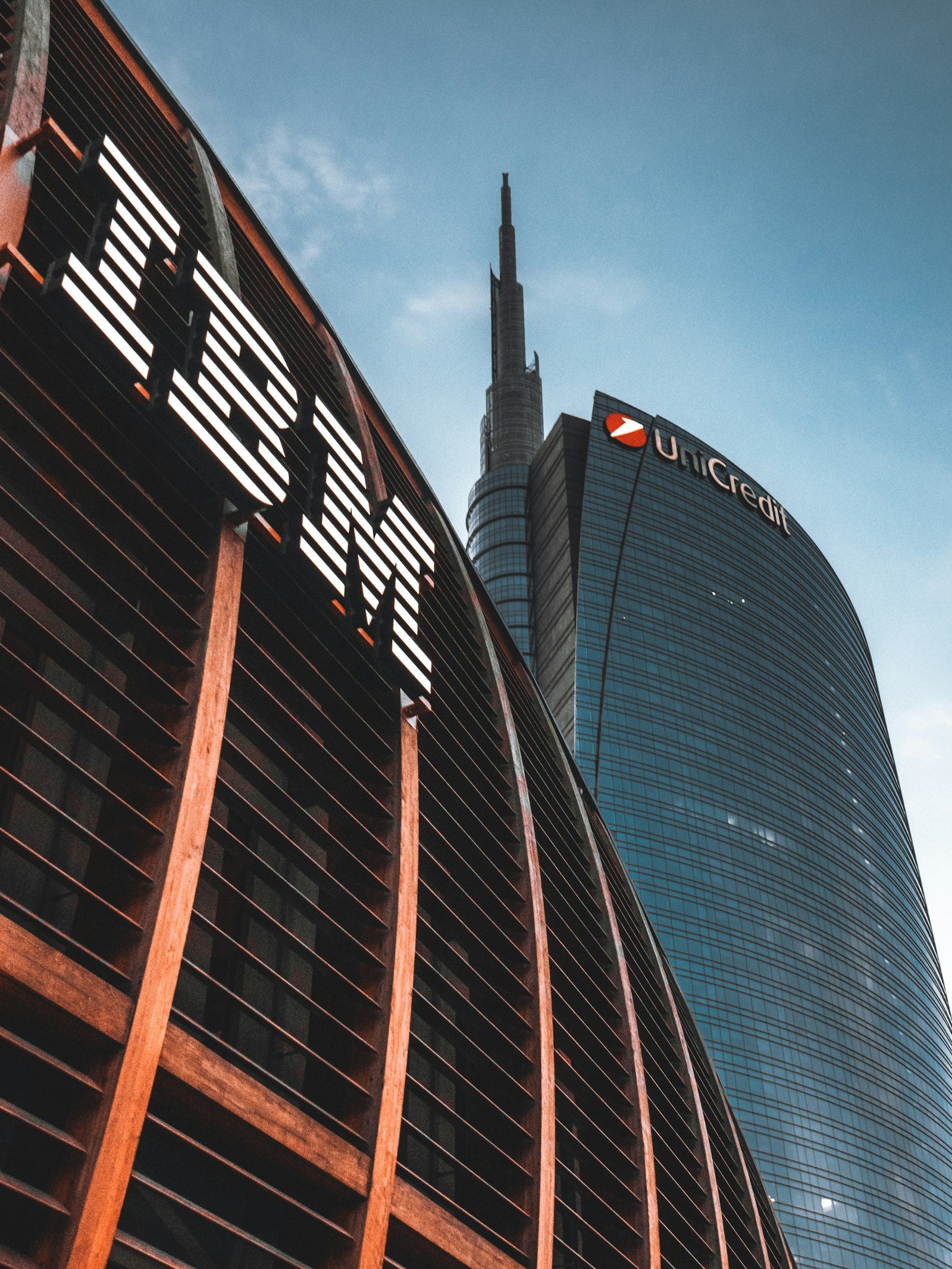 The image features the distinctive towers of the Unicredit Bank headquarters with the IBM logo prominently displayed in the foreground. The architectural design showcases a modern urban setting against a clear blue sky.