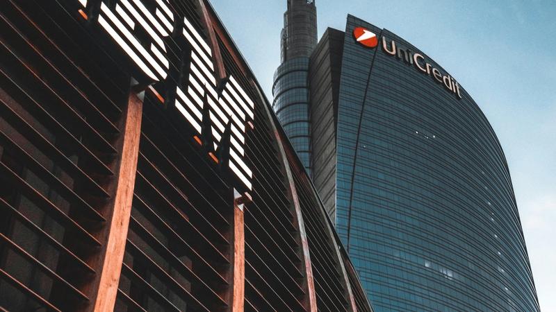 The image features the distinctive towers of the Unicredit Bank headquarters with the IBM logo prominently displayed in the foreground. The architectural design showcases a modern urban setting against a clear blue sky.
