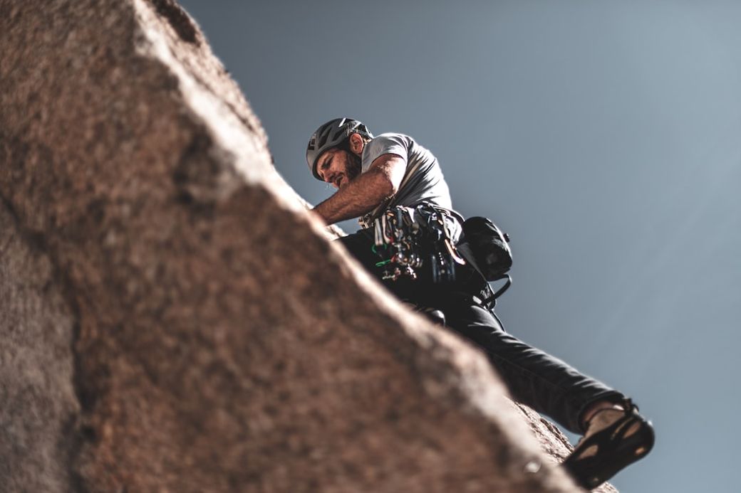 A climber is ascending a rocky cliff, showcasing the intensity and focus required for the sport. The image captures the climber from an elevated angle, emphasizing the challenging terrain and the climber's gear. — Credit: Photo by Patrick Hendry on Unsplash