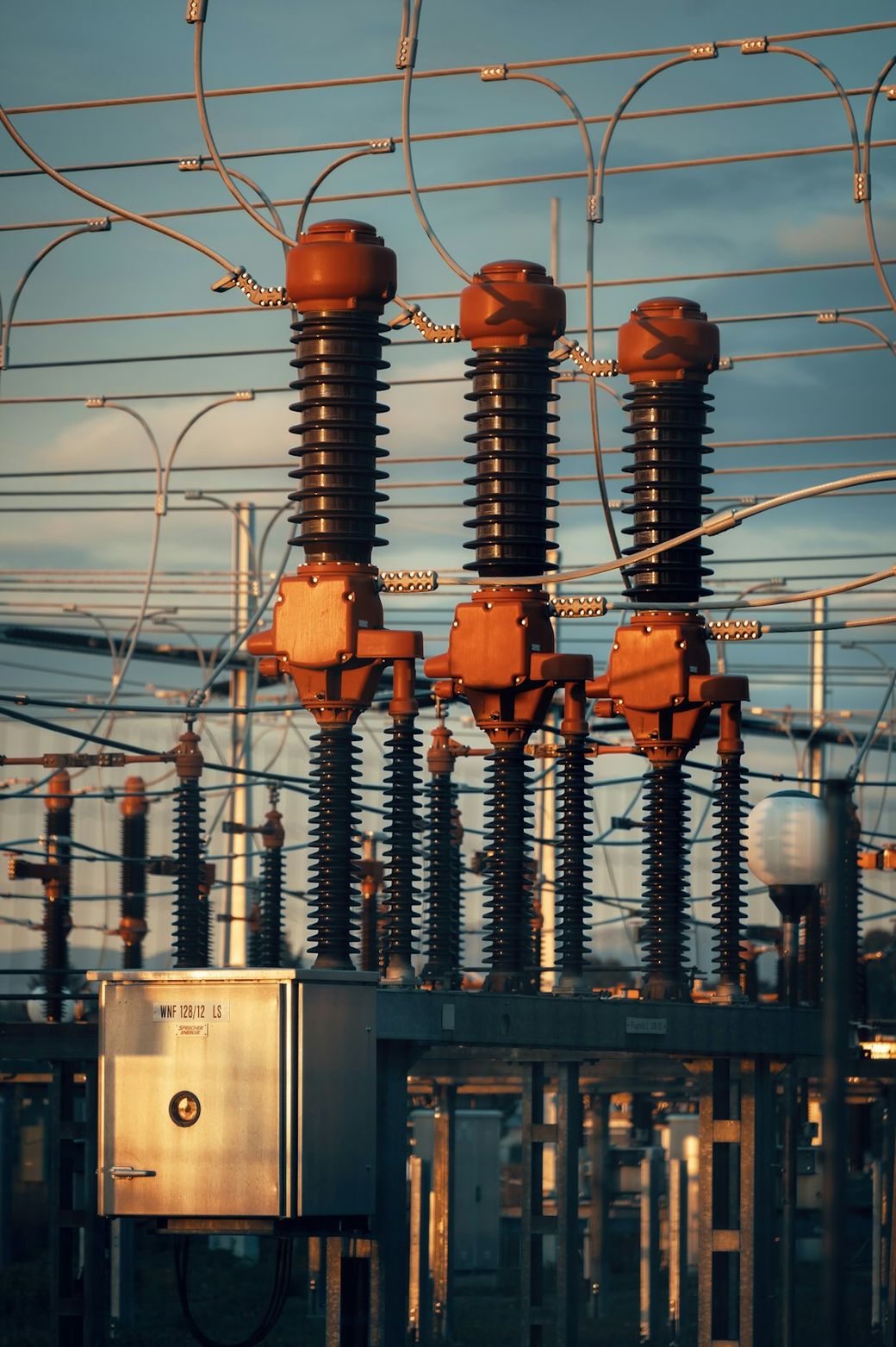 The image features an electrical substation with several high-voltage insulators and circuit components, indicating an energy distribution setup. The infrastructure showcases the intricate design of power transmission equipment under a clear sky. — Credit: Photo by Michael Pointner on Unsplash