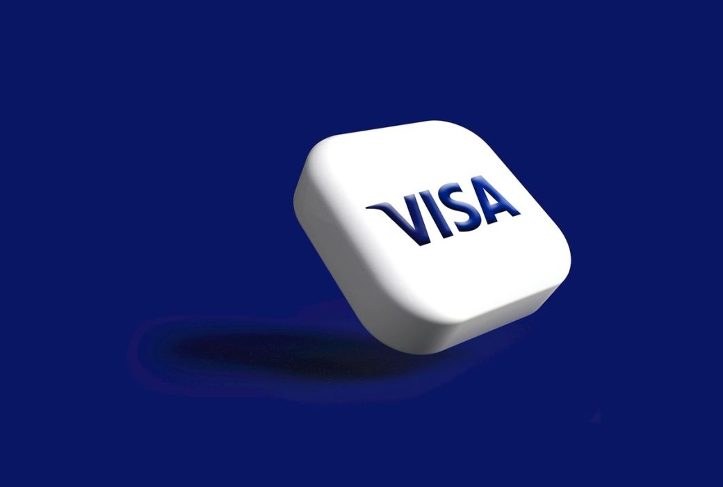 This image features a 3D rendering of a VISA logo on a solid blue background. The logo appears to be modern and clean, emphasizing brand recognition. — Credit: Photo by Rubaitul Azad / Unsplash