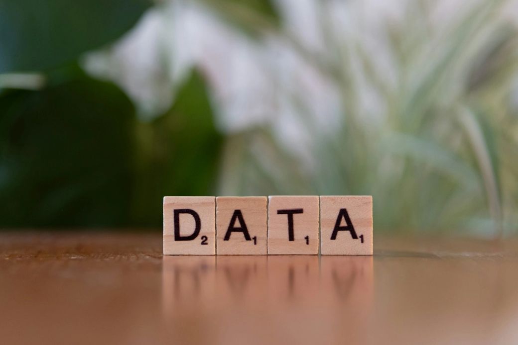 The image features wooden scrabble-like tiles spelling out the word 'DATA' on a wooden surface, set against a blurred green background. The composition emphasizes the concept of data in a visually appealing manner. — Credit: Photo by Markus Winkler / Unsplash