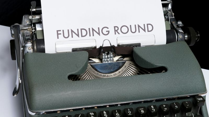 The image features a vintage typewriter with a sheet of paper that reads 'FUNDING ROUND' clearly visible. The typewriter is set against a neutral background, emphasizing the text on the page.