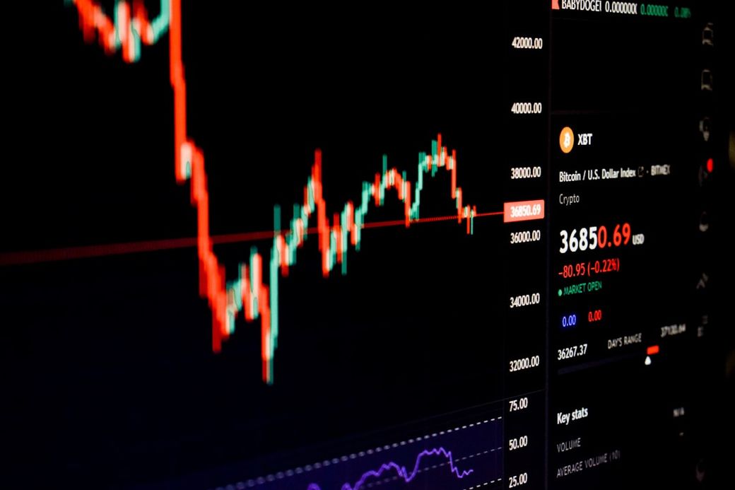 The image shows a close-up of a cryptocurrency trading interface featuring price charts and market data. The focus is on the fluctuating value of Bitcoin against the US Dollar, with technical indicators displayed in the background. — Credit: Photo by lonely blue on Unsplash