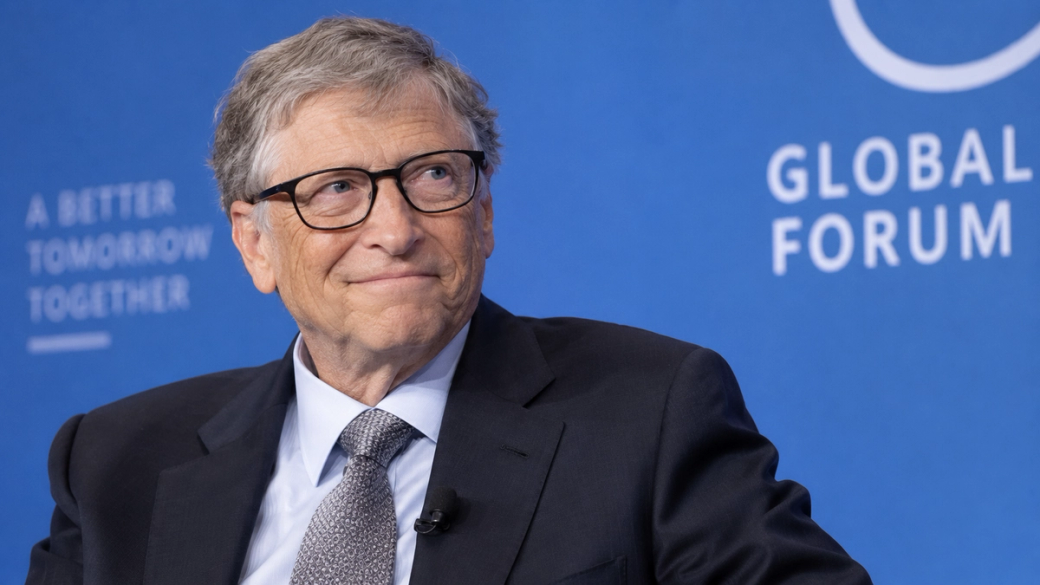 A close-up portrait of a man with glasses, smiling during a talk at a conference. The backdrop features a blue wall with text promoting a global forum focused on collaborative efforts for a better future.