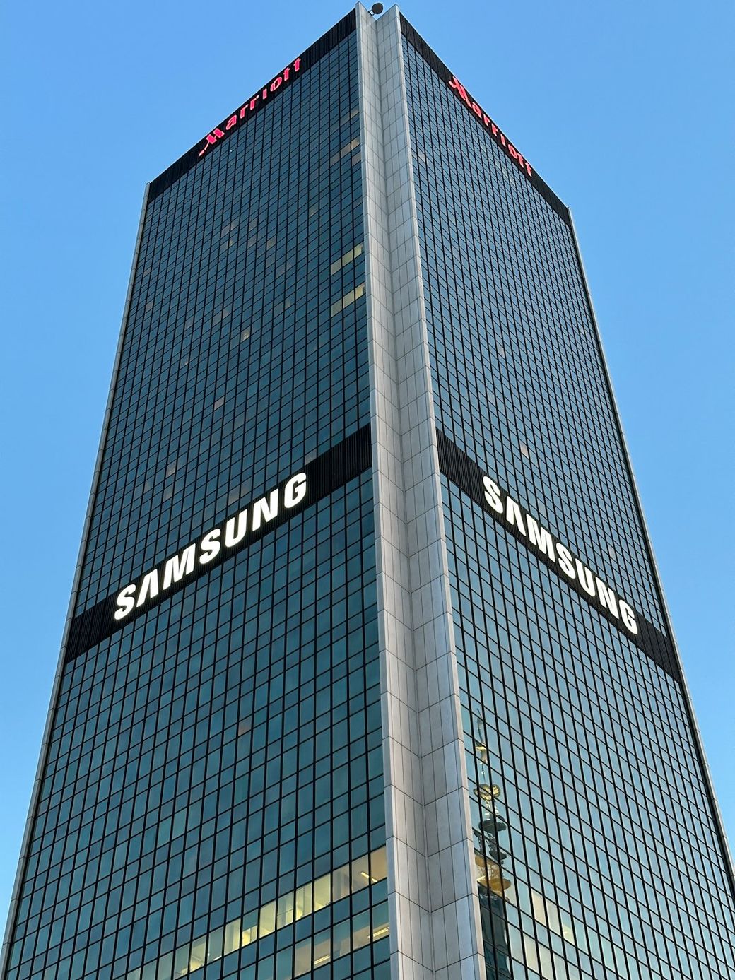 The image shows a tall, modern commercial building featuring prominent signage displaying the brand 'Samsung'. The building is set against a clear blue sky, enhancing its striking appearance. — Credit: Photo by Yurii Beresh on Unsplash
