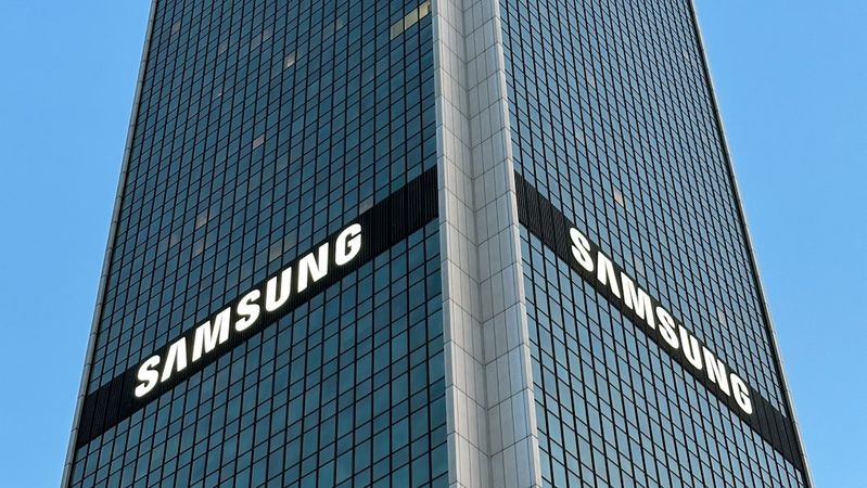 The image shows a tall, modern commercial building featuring prominent signage displaying the brand 'Samsung'. The building is set against a clear blue sky, enhancing its striking appearance.