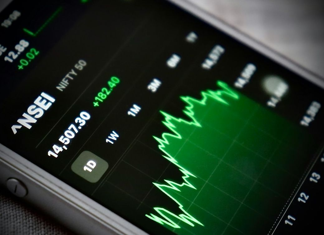 The image displays a close-up of a mobile phone screen showing the NSE (National Stock Exchange) market data. It features a graph indicating stock performance trends over different time frames with notable price changes. — Credit: Photo by Ramesh G on Unsplash