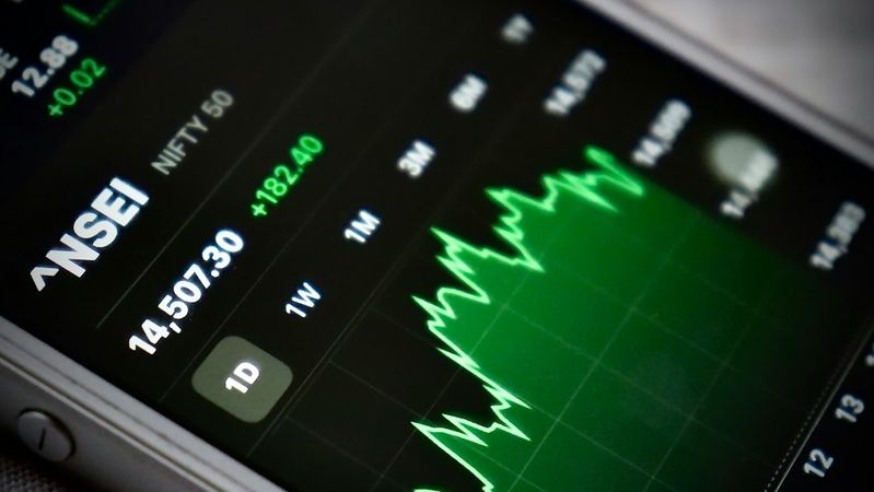 The image displays a close-up of a mobile phone screen showing the NSE (National Stock Exchange) market data. It features a graph indicating stock performance trends over different time frames with notable price changes.
