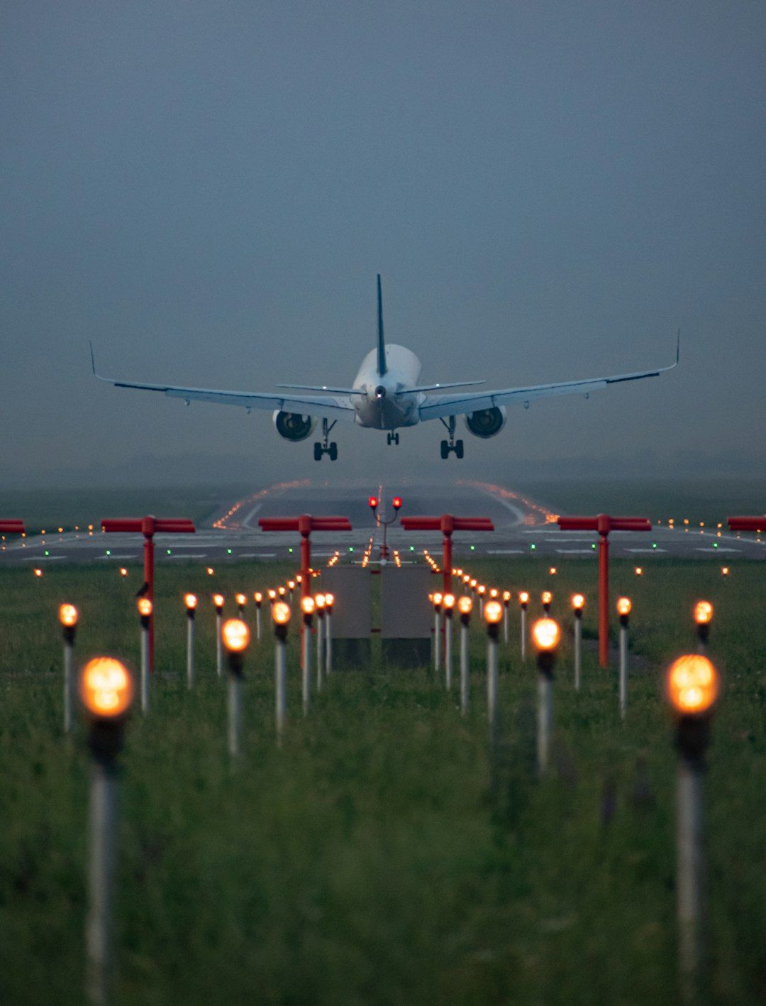 An airplane is captured as it approaches landing on a runway, surrounded by illuminated lights that guide its descent. The scene is set during twilight, showcasing a tranquil yet focused moment in aviation.