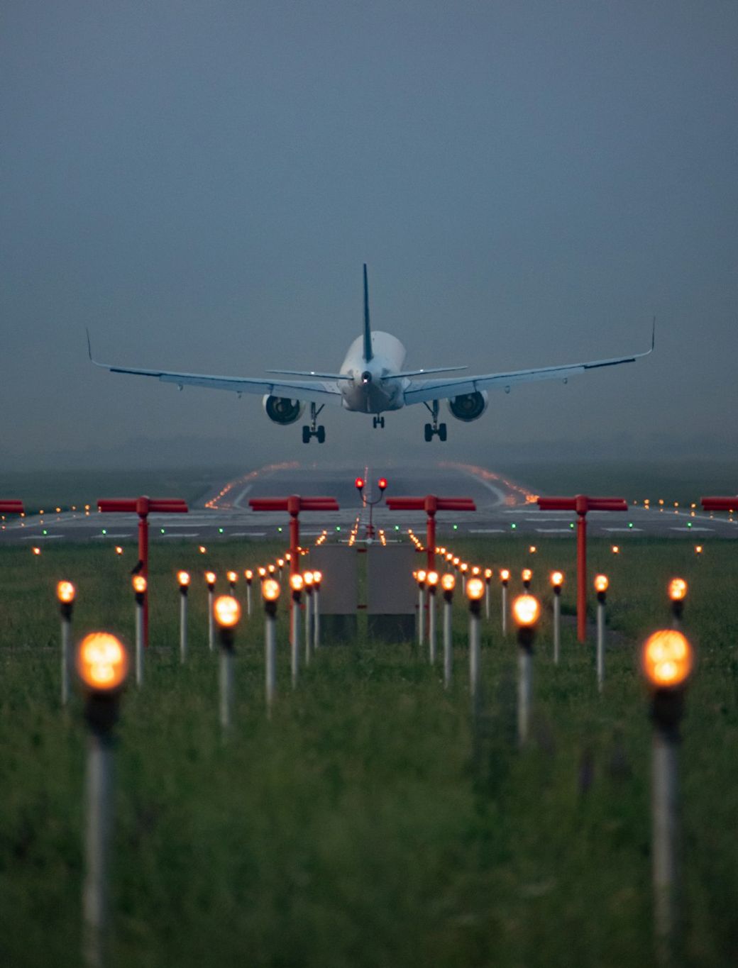An airplane is captured as it approaches landing on a runway, surrounded by illuminated lights that guide its descent. The scene is set during twilight, showcasing a tranquil yet focused moment in aviation. — Credit: Photo by Ilyas Dautov on Unsplash