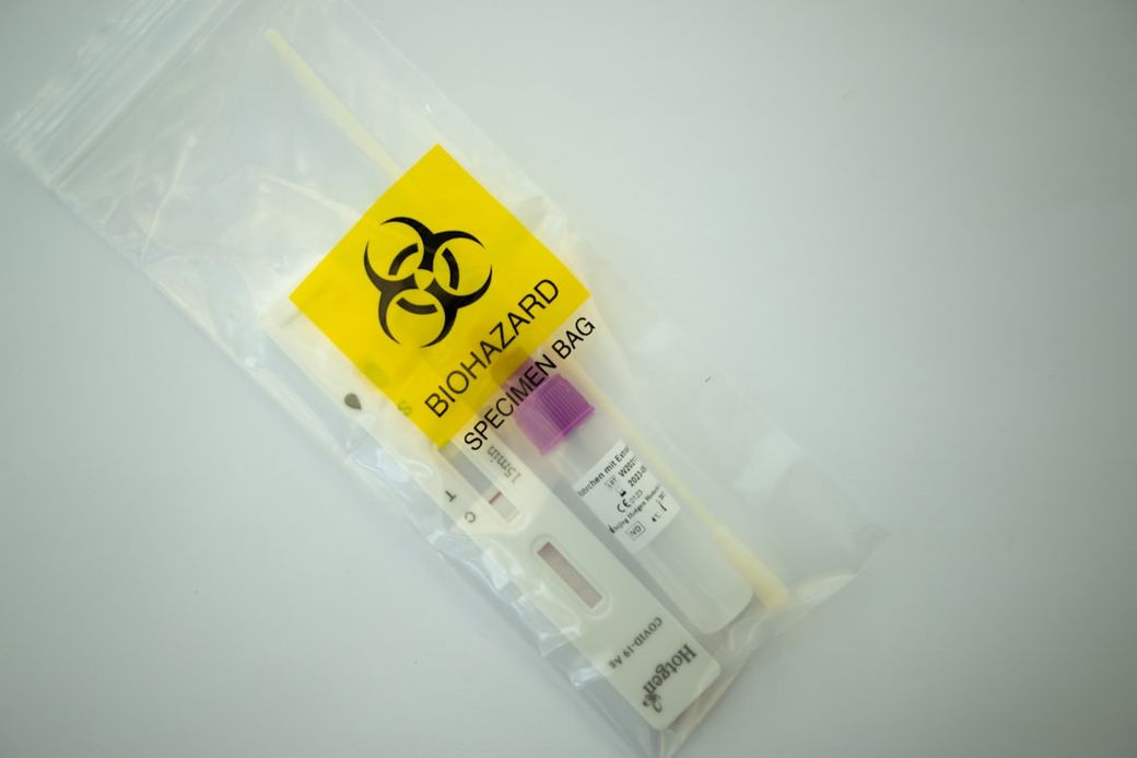 The image shows a sealed specimen bag labeled with a biohazard symbol, containing a testing kit. The bag is designed for safely transporting potentially hazardous biological materials. — Credit: Photo by Guido Hofmann on Unsplash