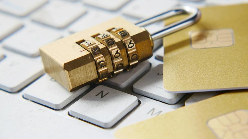The image features a combination padlock resting on a computer keyboard, surrounded by two gold credit cards. This visual emphasizes themes of security and financial protection in a digital context.