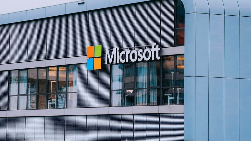 The image features the exterior of a modern building with large windows and a prominent Microsoft logo displayed on the wall. The architecture showcases contemporary design elements with horizontal lines.