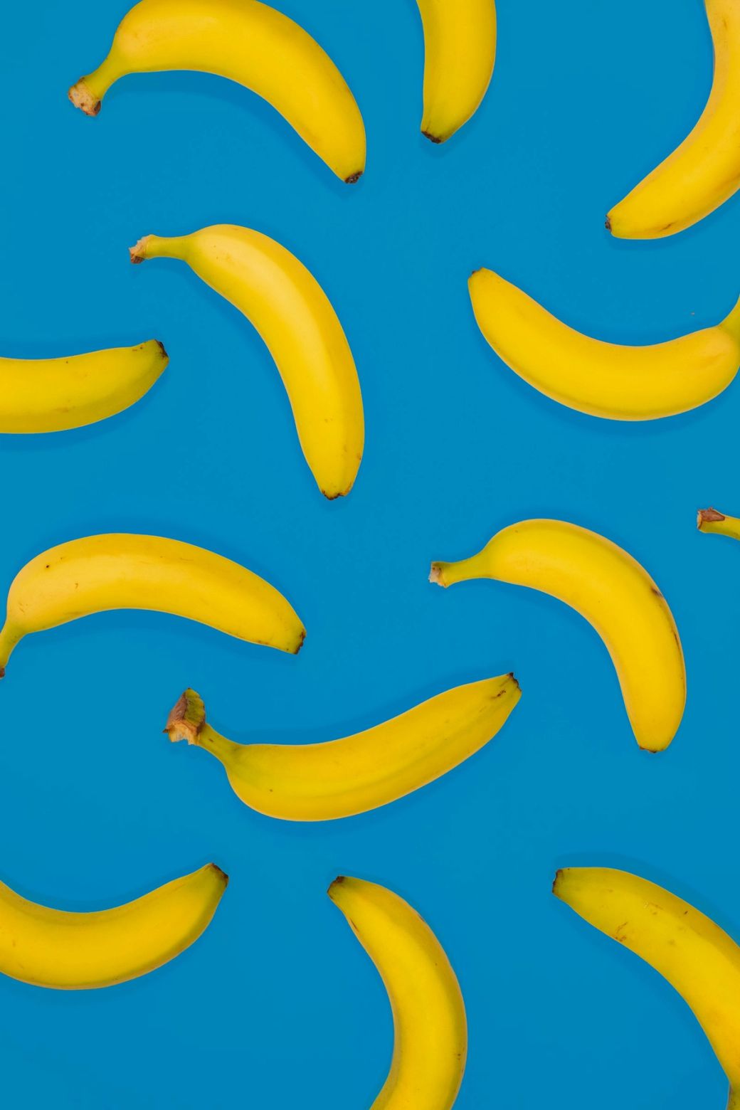 The image features several ripe bananas arranged against a bright blue background. The vibrant contrast highlights the yellow color of the bananas, creating a visually appealing composition. — Credit: Photo by matthew Feeney / Unsplash