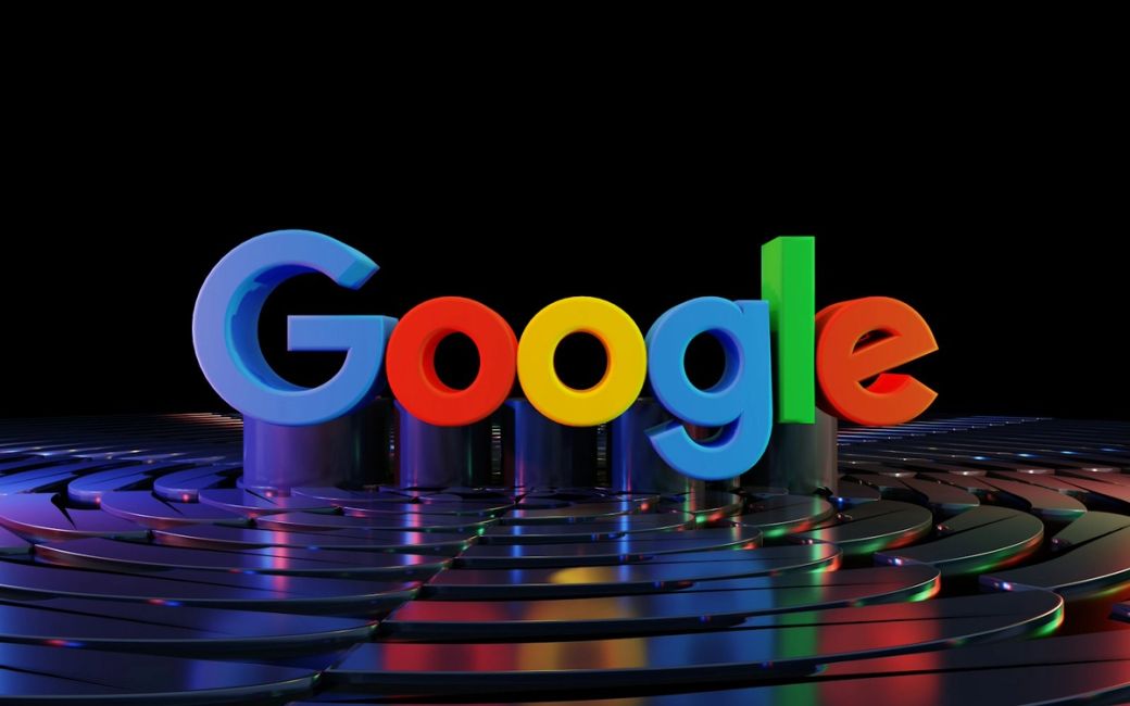The image features the colorful logo of Google, prominently displayed against a dark background. Beneath the logo, there is a reflective surface that creates a visually striking effect with various colors casting around. — Credit: Photo by BoliviaInteligente / Unsplash