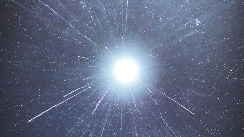 The image depicts a bright central light surrounded by a dark backdrop, creating an effect that resembles rays of light emanating outward. The composition suggests a cosmic or ethereal theme, evoking a sense of vastness and depth in space.