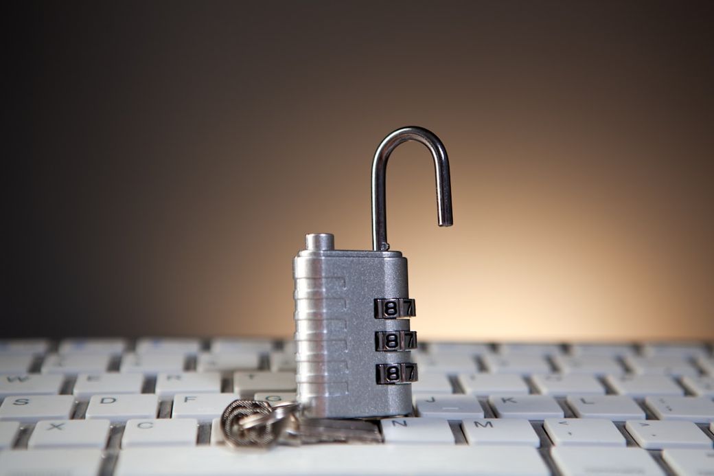 The image features a silver combination lock placed on a computer keyboard, with the lock appearing partially open. The blurred background suggests a focused setting on digital security themes. — Credit: Photo by Sasun Bughdaryan on Unsplash