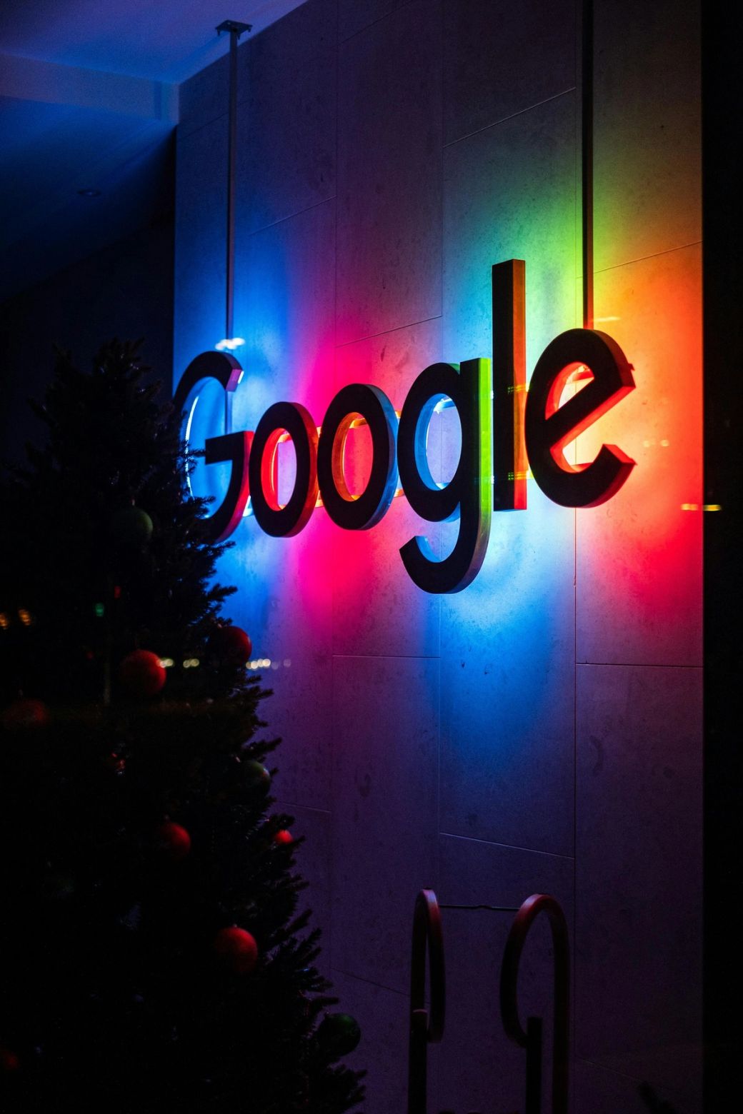 The image features the illuminated logo of Google, showcasing vibrant colors against a dark background. The setting appears to be a modern environment decorated for a festive occasion. — Credit: Photo by Sascha Bosshard / Unsplash