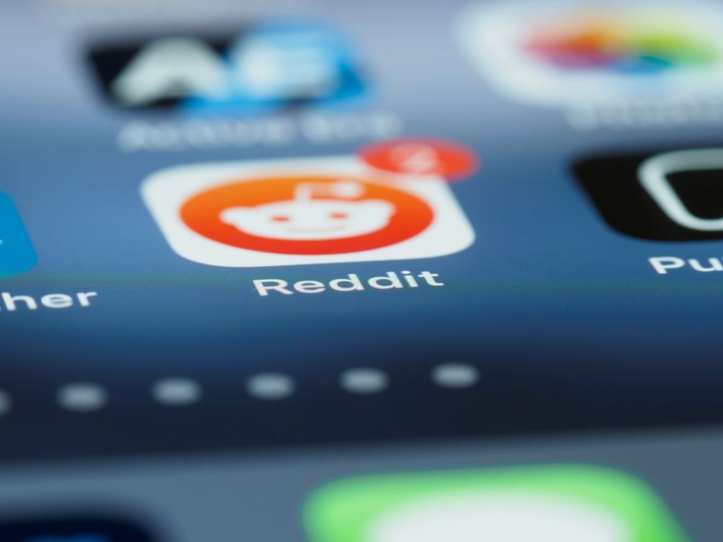 The image displays a close-up view of a smartphone screen showcasing various app icons, prominently featuring the Reddit app with a notification badge. The background is blurred, emphasizing the app's icon. — Credit: Photo by Brett Jordan on Unsplash