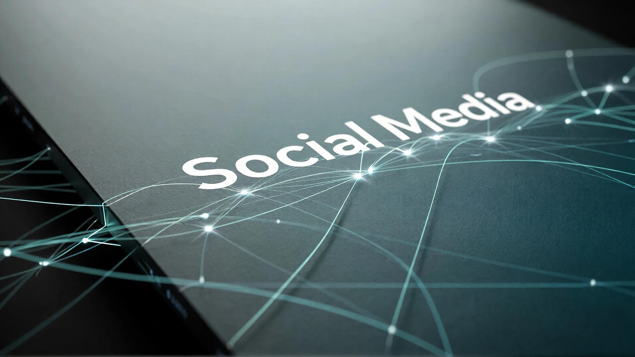 The image features a close-up view of a dark surface with the text 'Social Media' prominently displayed. The background includes a digital design with interconnected lines and light nodes, suggesting a technological theme.