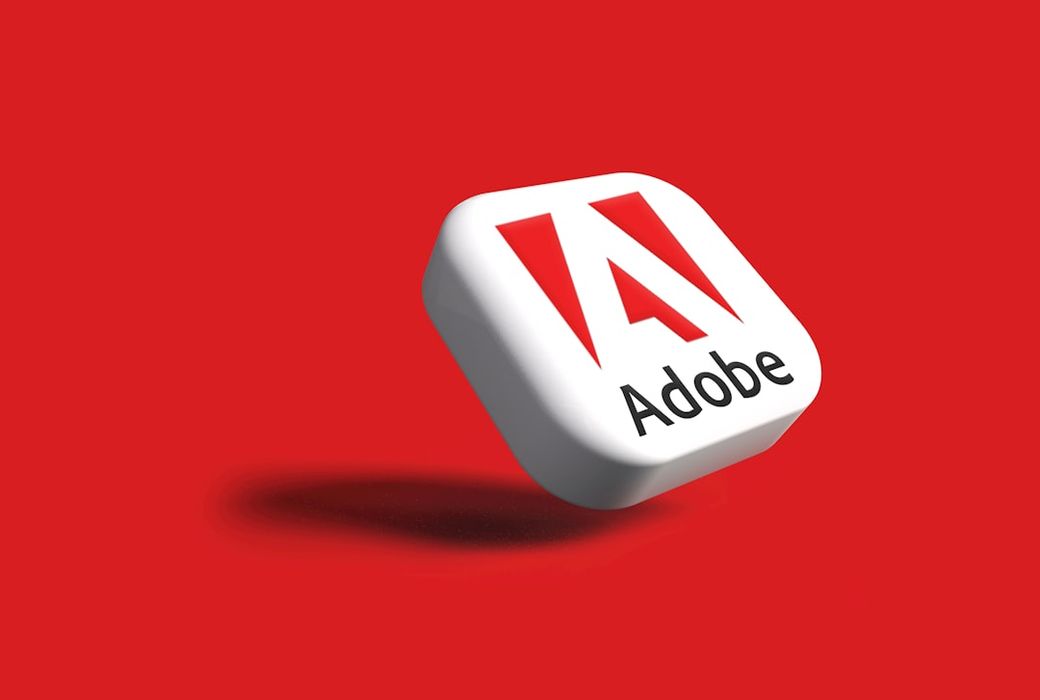 The image features a stylized 3D representation of the Adobe logo on a vibrant red background. The logo is prominently displayed, showcasing Adobe's brand identity. — Credit: Photo by Rubaitul Azad on Unsplash