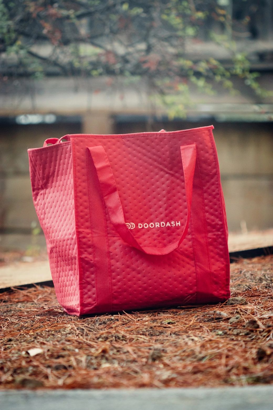 The image features a red insulated delivery bag prominently displaying the DOORDASH logo. The bag is designed for food delivery services, indicating its use in the logistics and food industry. — Credit: Photo by Griffin Wooldridge / Unsplash