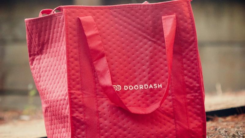 The image features a red insulated delivery bag prominently displaying the DOORDASH logo. The bag is designed for food delivery services, indicating its use in the logistics and food industry.