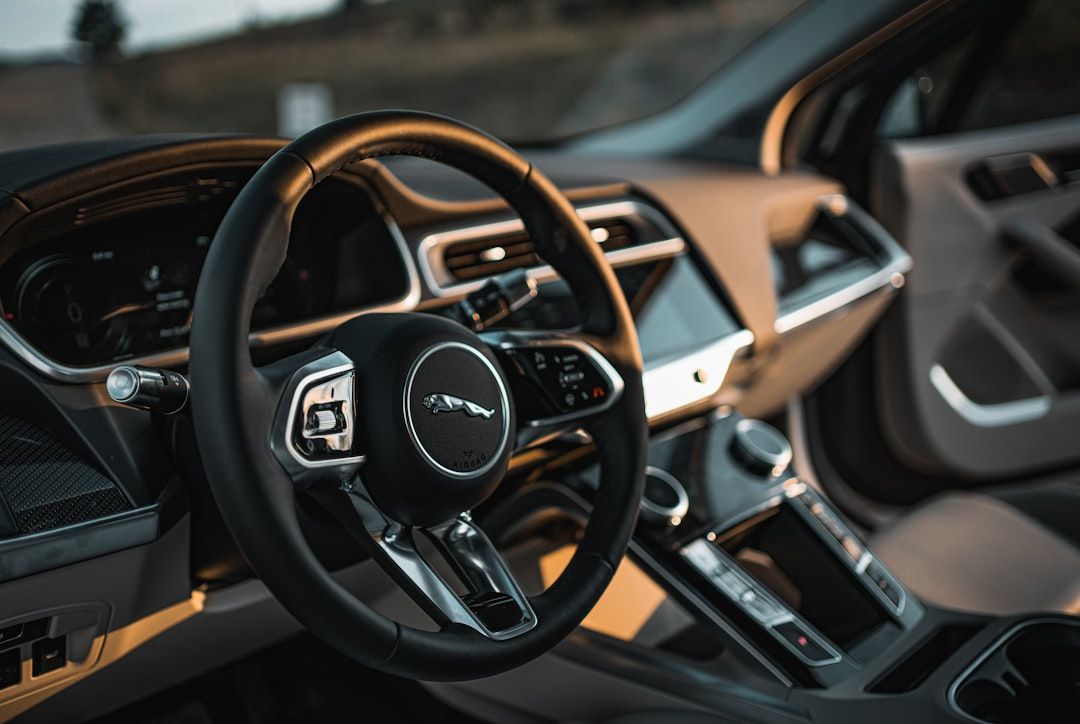 The interior of a luxury car featuring a modern dashboard layout and a circular steering wheel with a prominent logo. The dashboard includes digital displays and controls, showcasing a sleek design typical of high-end automobiles.