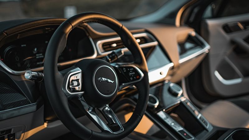 The interior of a luxury car featuring a modern dashboard layout and a circular steering wheel with a prominent logo. The dashboard includes digital displays and controls, showcasing a sleek design typical of high-end automobiles.