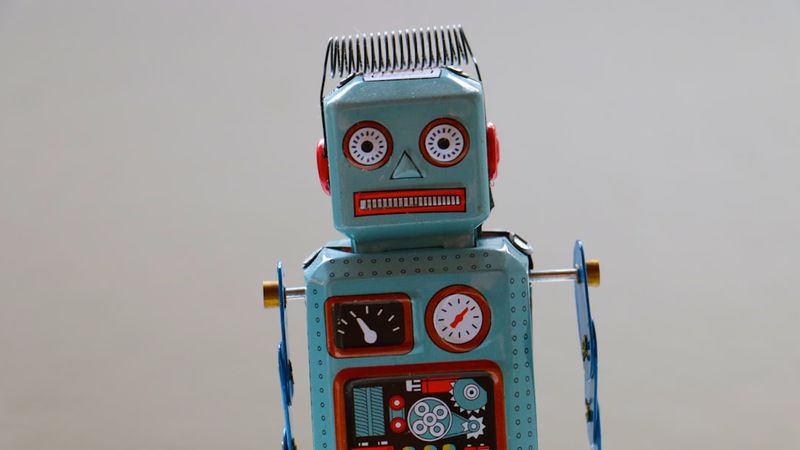 The image features a vintage toy robot with a retro design, displayed against a plain background. The robot has distinct facial features, including large eyes, and is adorned with mechanical details and dials.