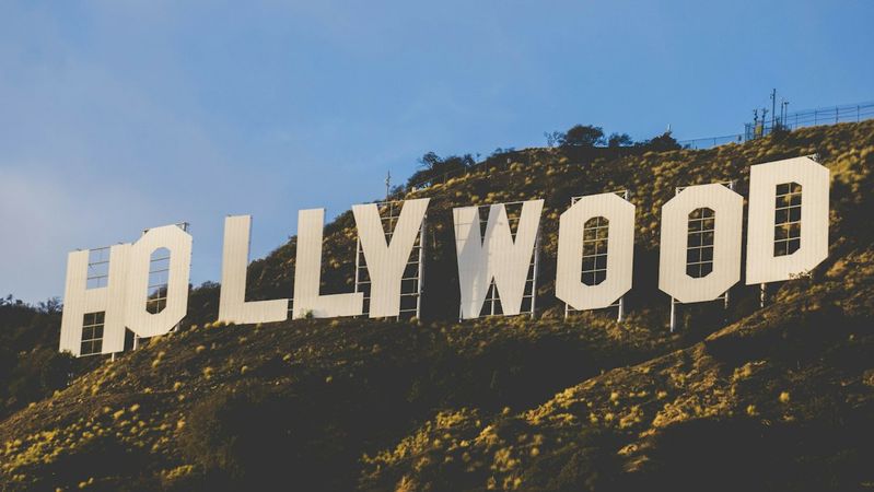 The iconic Hollywood sign is prominently displayed on a hillside, surrounded by greenery and under a clear blue sky. This landmark symbolizes the entertainment industry and is a major tourist attraction in Los Angeles.