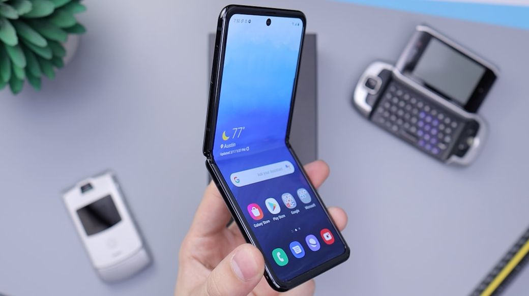 The image shows a person holding a modern, foldable smartphone with a colorful home screen. In the background, there are older mobile devices, including a flip phone and a QWERTY keyboard phone, emphasizing the evolution of technology. — Credit: Photo by Daniel Romero on Unsplash