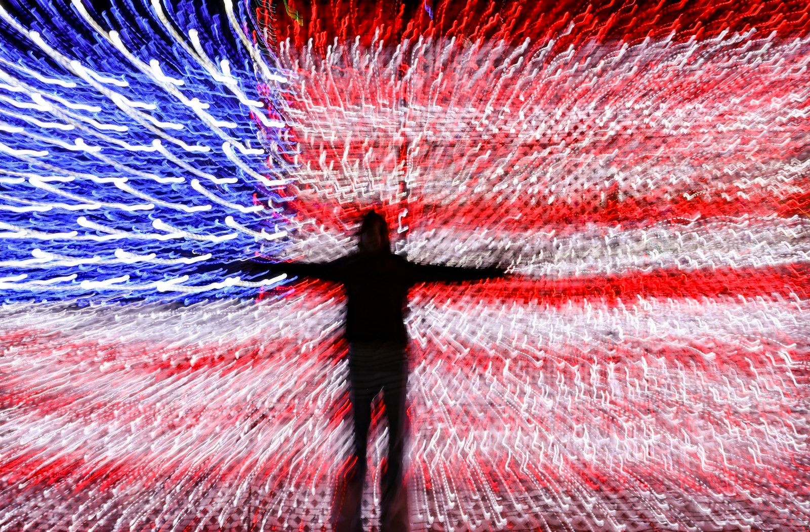 The image features a blurred figure standing against a vibrant backdrop designed to resemble the American flag, with swirling lights creating a dynamic effect. The contrast of the red, white, and blue colors conveys a sense of movement and energy.